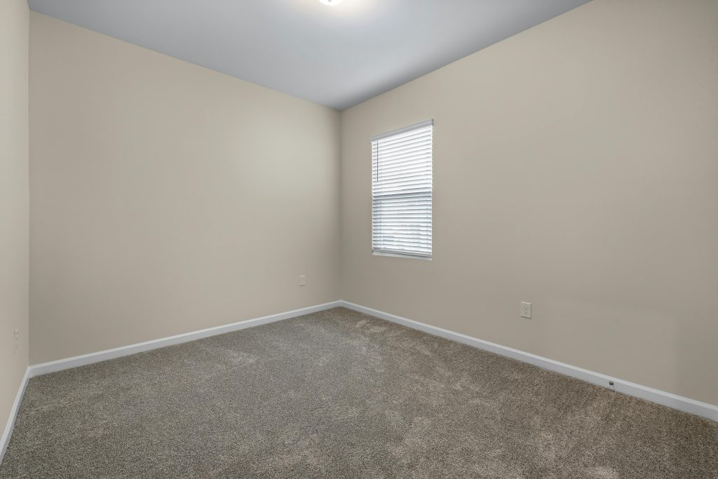 Explore a minimalist empty room featuring carpet flooring and natural light through a window. Perfect for real estate and design concepts.