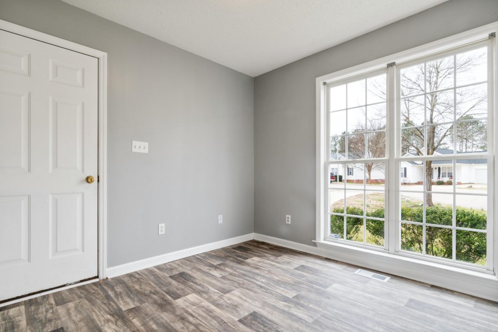 Bright and spacious empty room with wooden flooring and large window, perfect for residential property listings.